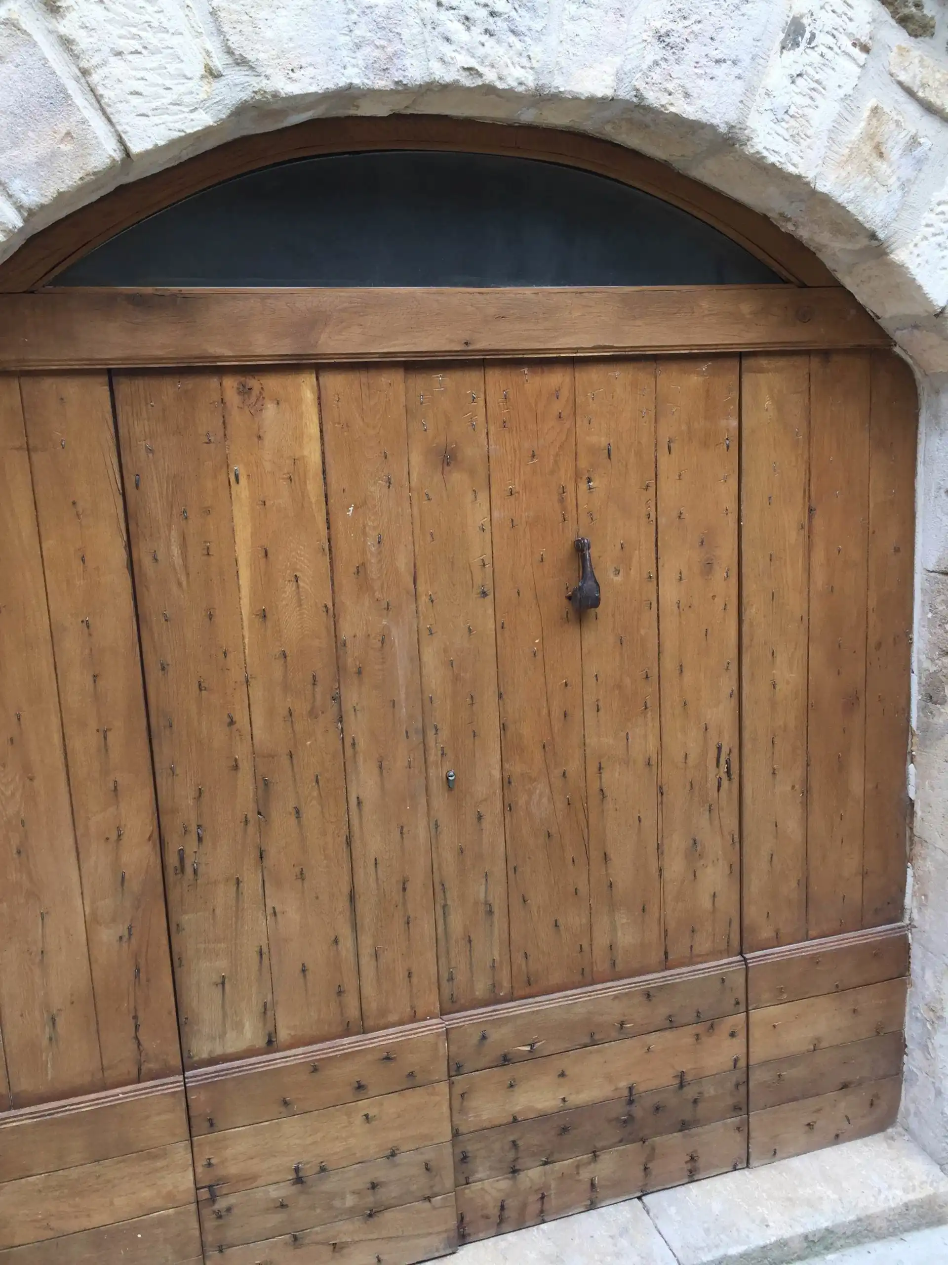 Porte en bois massif sur mesure intégrée dans une ouverture voûtée en pierre restaurée