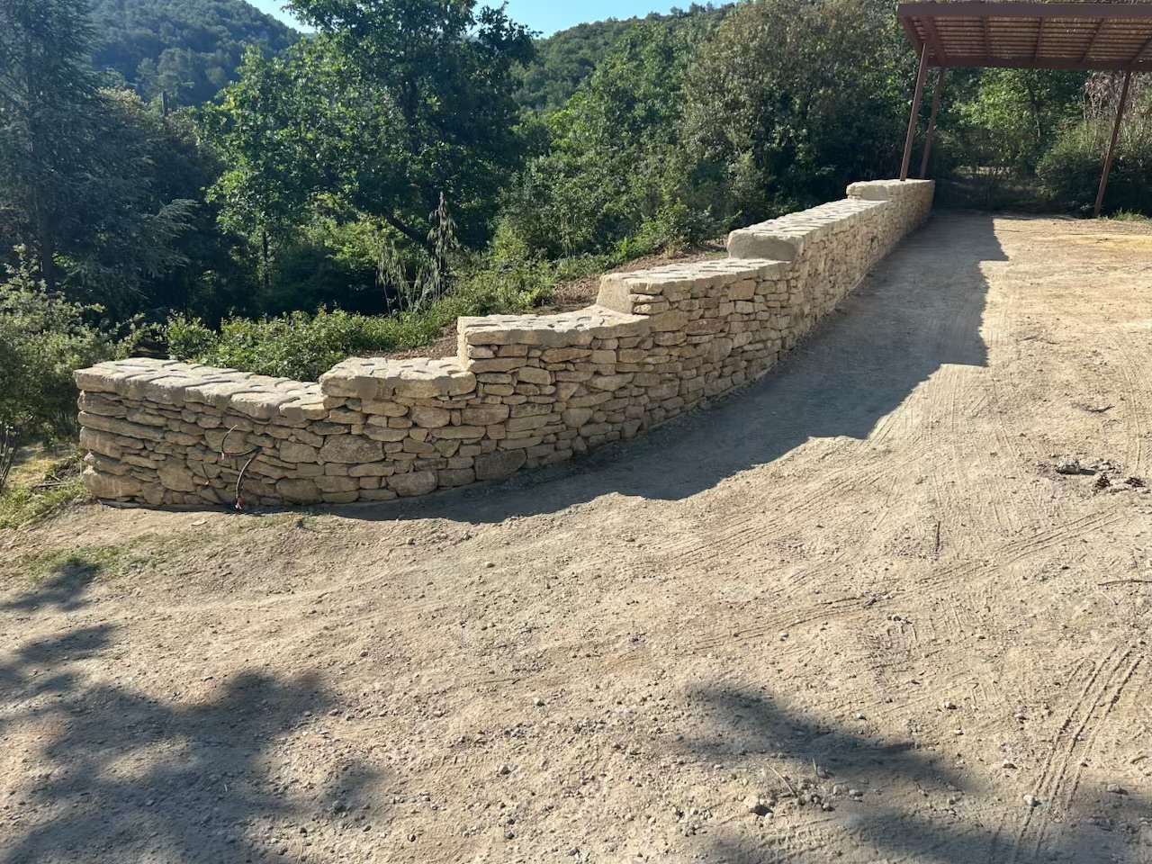 Le nouveau mur en pierre sèche double face délimite et valorise la propriété. Son tracé courbe et ses différences de hauteur accompagnent naturellement le relief du terrain.